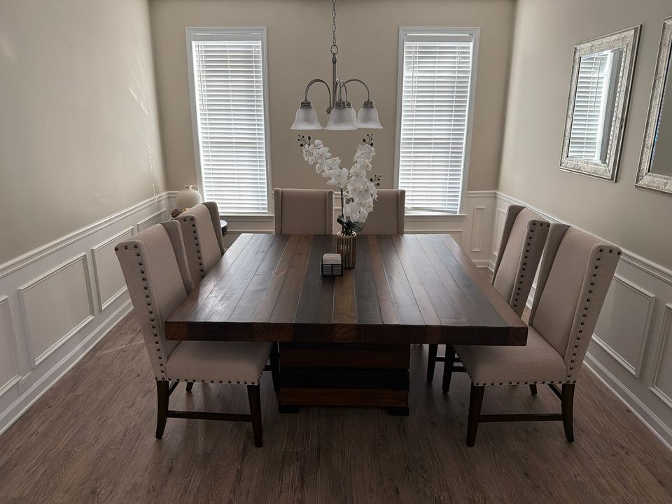 Formal dining room with a dark wood table, cream upholstered chairs, a chandelier and white wainscoting